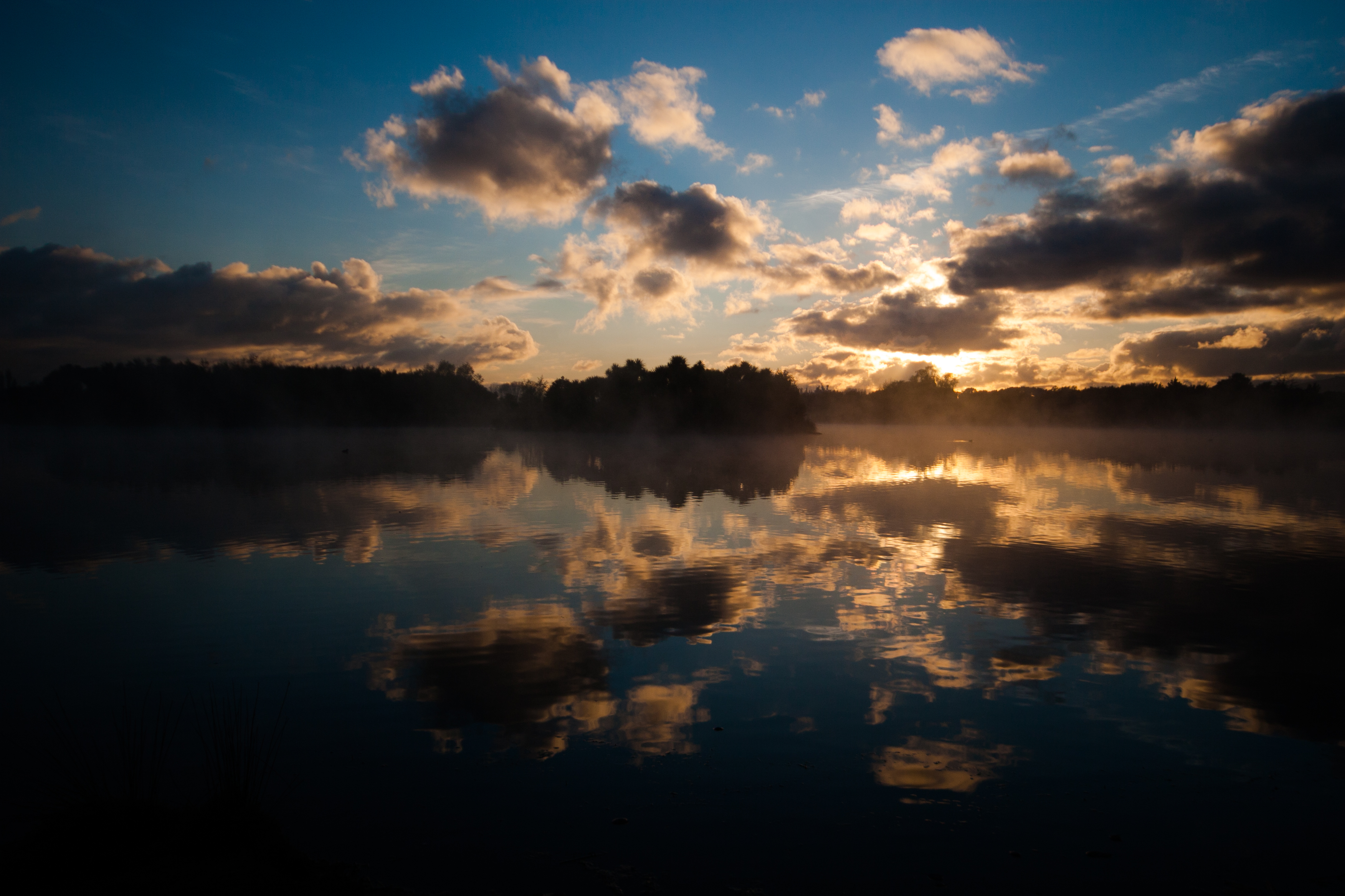 reflections of clouds in a pond with sun poking out from behind the clouds at sunrise