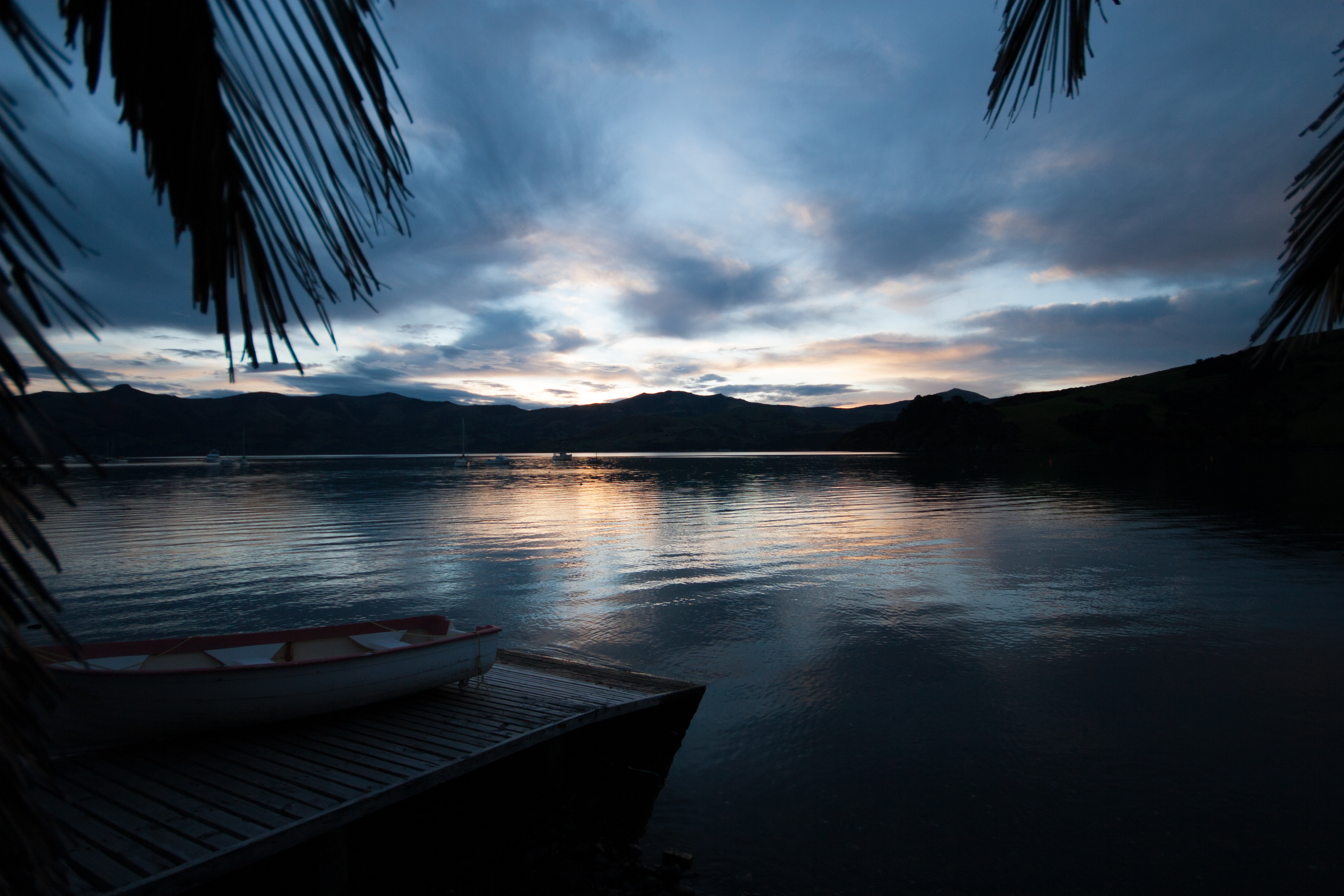 sunsetting over the mountains in front of a lake with palm trees just inside the frame a boat waiting on a ramp