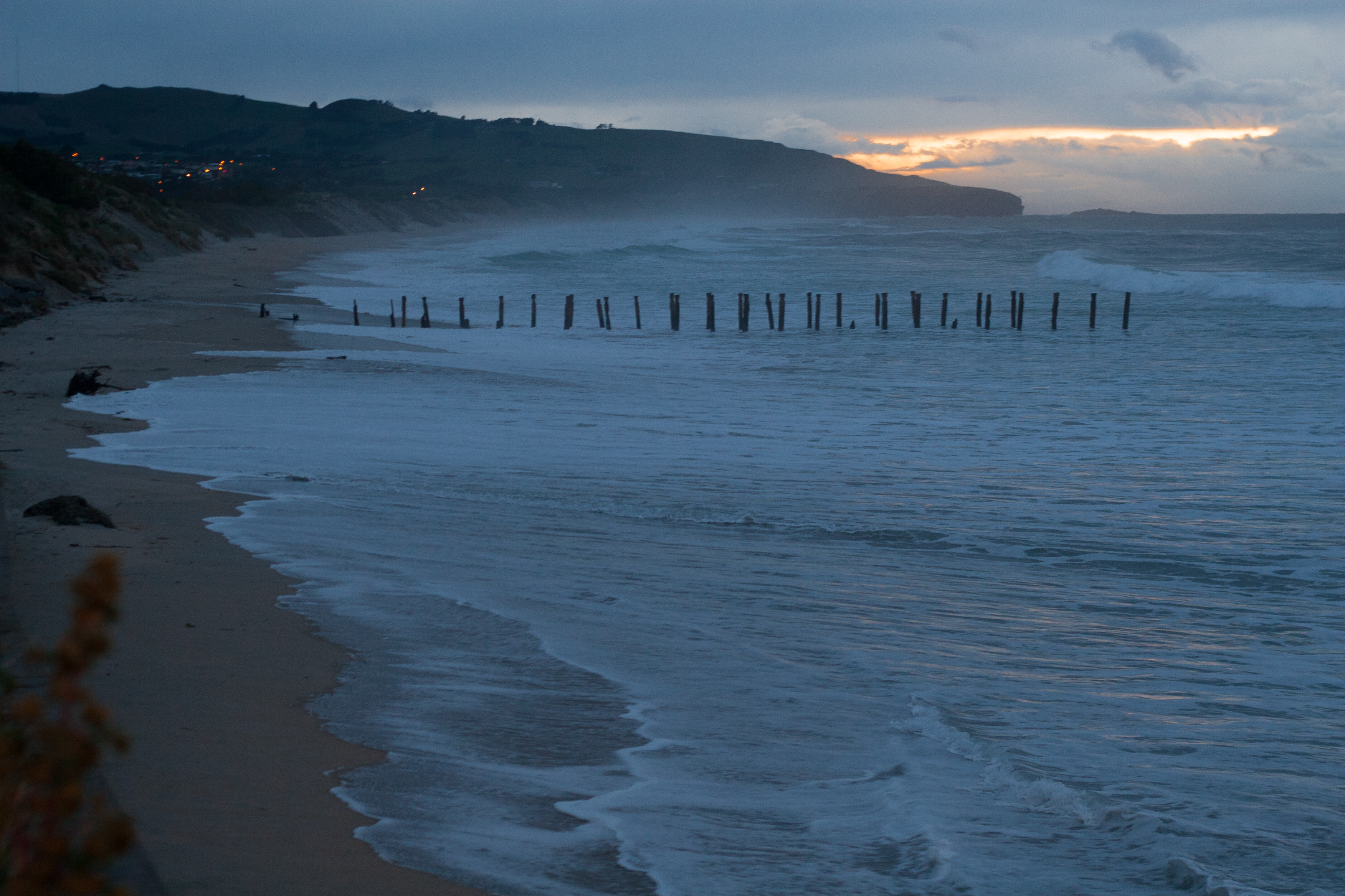 the remains of an old pier visible as the sun rises over the hill near the ocean