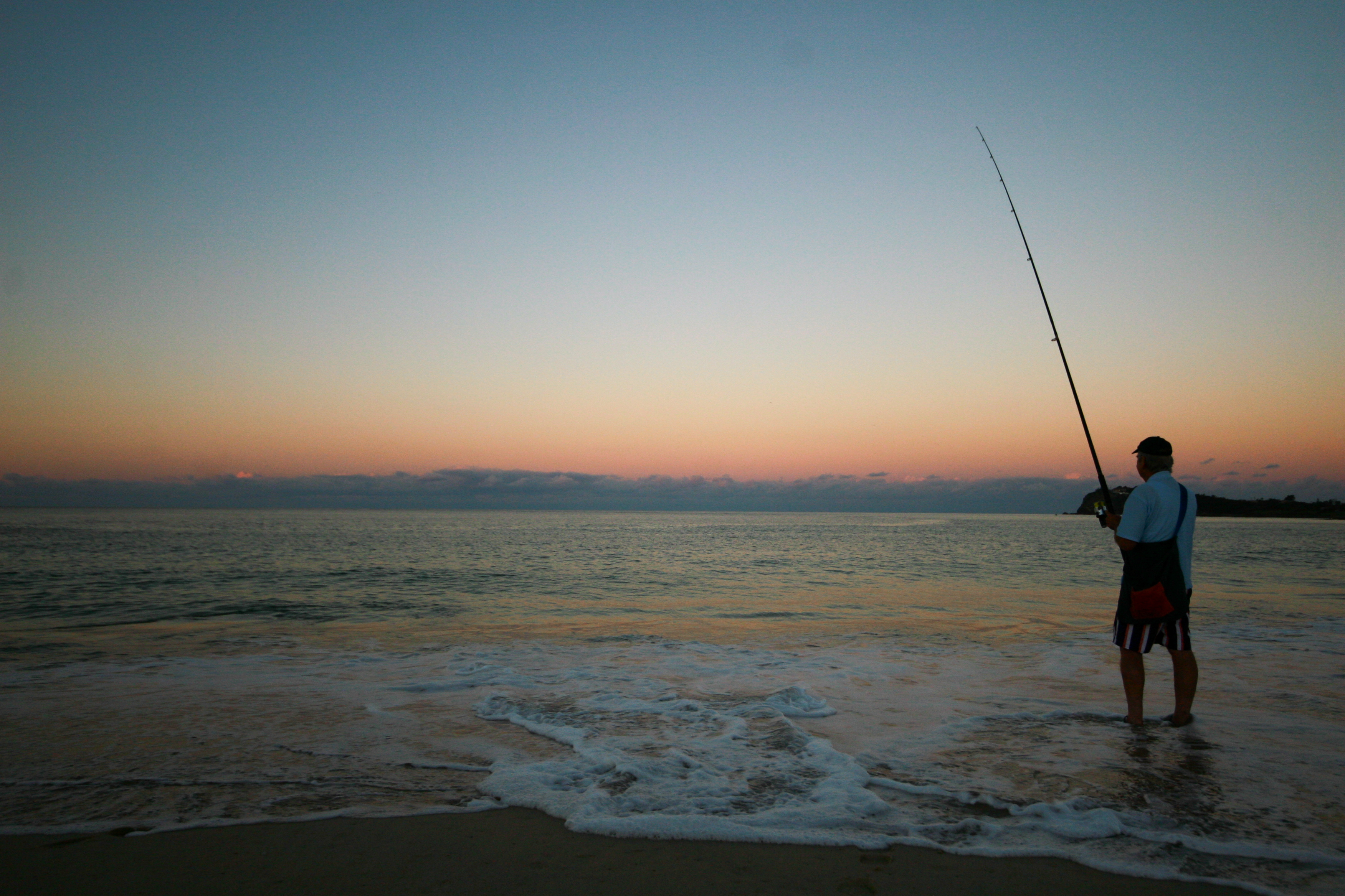 man fishing on the beach at sunset